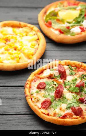 Drei verschiedene Pizzasorten auf einem schwarzen Holztisch. Vertikales foto. Draufsicht Stockfoto