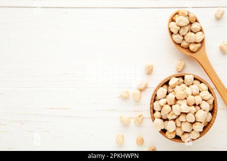 Ungekochte Kichererbsen in Holzlöffel und Schüssel auf weißem Hintergrund. Draufsicht Stockfoto