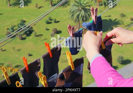 Die Hand einer Frau, die Socken an der Wäscheleine hängt, mit Wäscheklammern im oberen Stockwerk Stockfoto