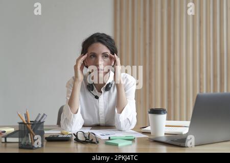 Frustrierte Geschäftsfrau, die sich müde fühlt, während sie am Tisch im Büro sitzt, über Problemlösungen bei der Arbeit nachdenkt, junge gestresste italienische Frauen beschäftigen Stockfoto