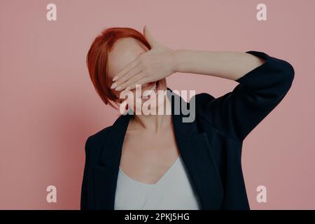 Süße positive Ingwer-Frau, die Hand vor dem Gesicht hält, die Augen verdeckt, in Erwartung auf etwas wunderbares, wartet auf Überraschung von ihrem Freund Stockfoto