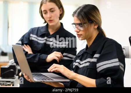Ingenieurinnen, die Laptopprüfungen durchführen und Robotermaschinen bedienen Stockfoto