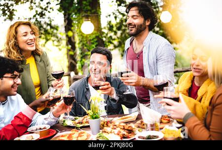 Glückliche Männer und Frauen, die Spaß beim Trinken im Garten des Weinbauernhofs haben - Lebensstil für Speisen und Getränke, bei dem Freunde aus verschiedenen Altersgruppen Zeit miteinander verbringen Stockfoto