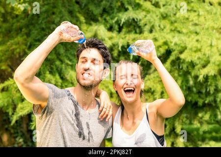 Sportliches Paar erfrischt sich nach dem Lauftraining im Park mit kaltem Wasser - Sport Fitness junge, fröhliche Models machen eine Pause nach dem Joggen in der Natur Stockfoto