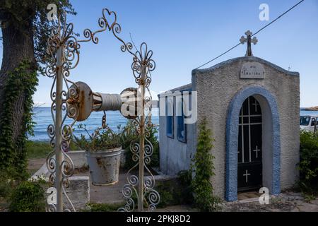 Saint Marina (Agia Marina) steht über der Tür. Blaue Kapelle mit Kreuz und Engel auf dem Dach, erbaut in einem wunderschönen kleinen Garten an der Küste. Verwandte Stockfoto