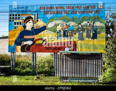 Eine vietnamesische Kommunistische Partei malte Propagandafilter, auf denen ethnische Minderheiten dargestellt werden, die Gongs spielen und einen Traktor fahren. Die Plakatwand drängt Stockfoto