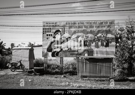 Eine vietnamesische Kommunistische Partei malte Propagandafilter, auf denen ethnische Minderheiten dargestellt werden, die Gongs spielen und einen Traktor fahren. Die Plakatwand drängt Stockfoto