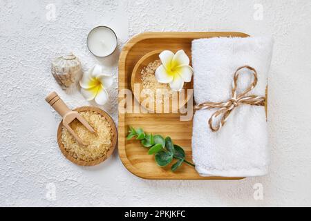 Spa- und Badezimmerzubehör auf Holztablett, Meersalz auf Holzlöffel, Handtuch, Meerstein, weiße Orchideen. Spa- und Massageprodukte bilden die Konzeption. Stockfoto