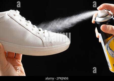 Anwendung eines wasserabweisenden hydrophoben Sprays auf weiße Frauenschuhe. Schutz der Schuhe vor Feuchtigkeit, Schmutz und unangenehmem Geruch. Stockfoto