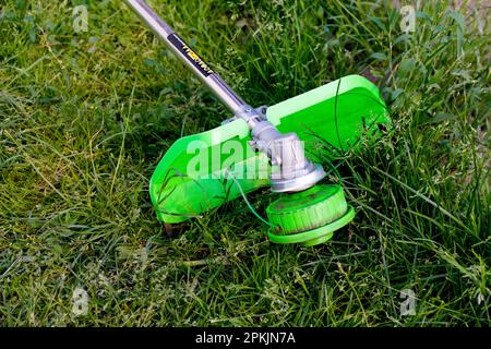 Unschärfe-Effekt-Rasentrimmer. Ein Mann, der das Gras mäht. Außenansicht eines Rasentrimmermähers, der Gras in einem unscharfen Naturhintergrund schneidet. Hausarbeit. Abgeschnitten Stockfoto