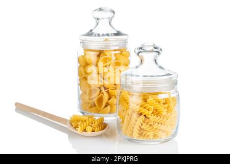 Fusilli und Conchiglioni in Glasgefäß isoliert auf weißem Hintergrund. Zwei verschiedene Arten von roher Pasta in Glasgefäßen, Zutaten zum Kochen, traditionell Stockfoto
