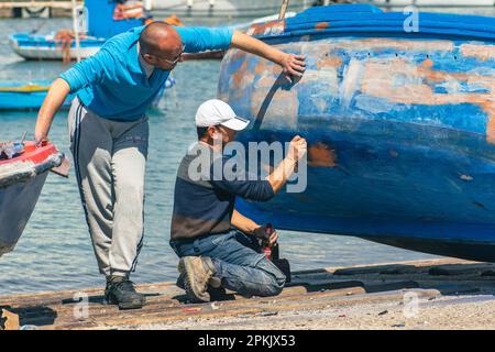 Fischer reparieren und streichen ein altes hölzernes Fischerboot am Hafenkai in Bari, Apulien Italien Stockfoto