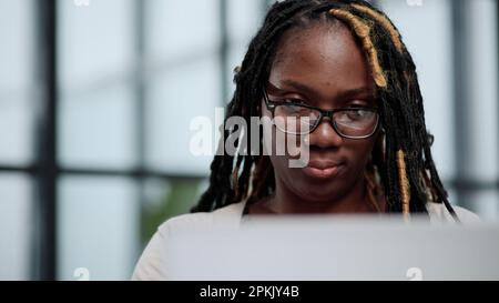 Ein Freiberufler arbeitet per Fernzugriff auf einem Laptop in einem Browser an einem neuen Projekt für die Arbeit. Lockiges schwarzes Haar. Stockfoto