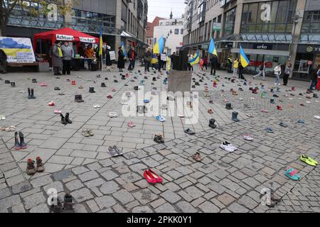 Jena, Deutschland. 08. April 2023. Kinderschuhe und Menschen mit ukrainischen Flaggen stehen auf einem Platz im Zentrum der Stadt. Mit der Aktion sammeln Frauen, die aus der Ukraine geflohen sind, Spenden für die Eltern von Kindern, die im Krieg getötet wurden. Kredit: Bodo Schackow/dpa/Alamy Live News Stockfoto