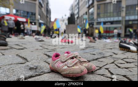 Jena, Deutschland. 08. April 2023. Kinderschuhe und Menschen mit ukrainischen Flaggen stehen auf einem Platz im Zentrum der Stadt. Mit der Aktion sammeln Frauen, die aus der Ukraine geflohen sind, Spenden für die Eltern von Kindern, die im Krieg getötet wurden. Kredit: Bodo Schackow/dpa/Alamy Live News Stockfoto