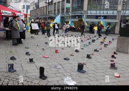 Jena, Deutschland. 08. April 2023. Kinderschuhe und Menschen mit ukrainischen Flaggen stehen auf einem Platz im Zentrum der Stadt. Mit der Aktion sammeln Frauen, die aus der Ukraine geflohen sind, Spenden für die Eltern von Kindern, die im Krieg getötet wurden. Kredit: Bodo Schackow/dpa/Alamy Live News Stockfoto