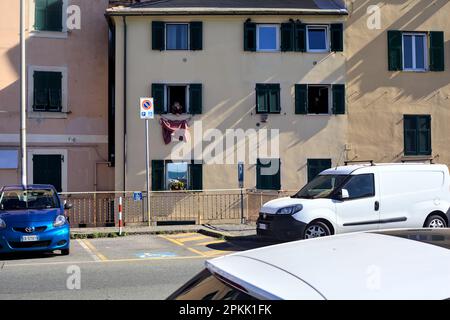 Fassade eines Gebäudes mit hängenden Kleidern und einer Frau am Fenster, von einem Gehweg am Rand einer Straße aus gesehen Stockfoto