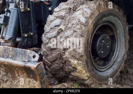 Radtraktor mit Schaufel räumt an bewölkten Regentagen den Boden frei. Schmutzige Bulldozer-Schaufel Nahaufnahme... Stockfoto