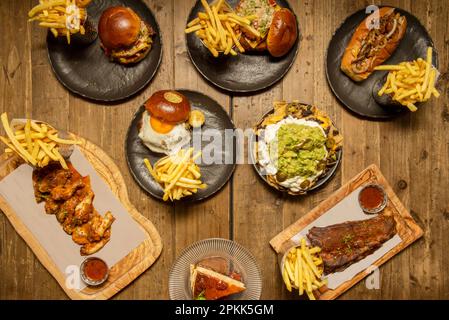 Set aus Fast-Food-Gerichten mit vielen Burgern, grillrippchen, Büffelflügeln, Käsekuchen und Nachos mit Guacamole Stockfoto