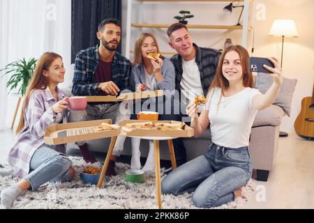 Frau macht Selfie. Eine Gruppe von Freunden feiert zusammen drinnen Stockfoto