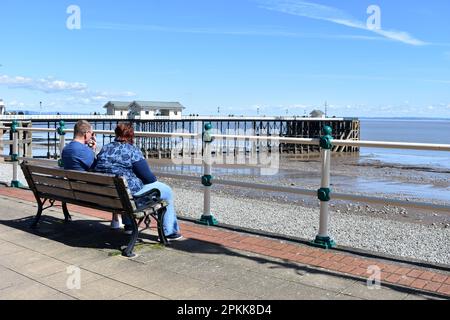 Ein Paar, das auf einer Bank neben Penarth Pier, Penarth, Wales sitzt Stockfoto