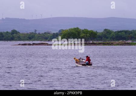 Ein Mann mit seinem Hund auf einem Boot, das auf einem See in Irland fischt Stockfoto