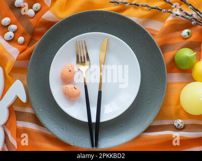 Ostertisch mit Eiern, Häschen- und Weidenzweig auf orangefarbenem Hintergrund Stockfoto