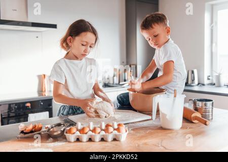 Ich mache Süßigkeiten. Ein kleiner Junge und ein Mädchen, die in der Küche Weihnachtskekse zubereiten. Stockfoto