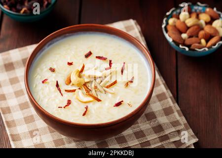 Reispudding in Tonschüssel serviert. Indischer Reisheer mit Nüssen auf Holzhintergrund. Beliebtes Ramadan-Gericht. Draufsicht Stockfoto