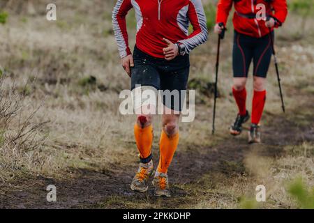 Zwei Läufer laufen im Schlammlauf ein Sportrennen, das Knie ist vom Sturz bedeckt Stockfoto