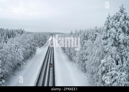 Draufsicht eines Autos, das auf einer vereisten Straße im verschneiten Wald in Lappland, Finnland, Europa fährt Stockfoto