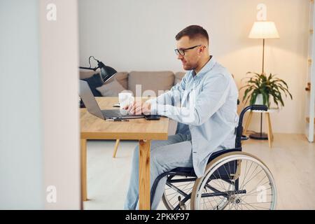 Arbeiten mit einem Laptop. Behinderter im Rollstuhl ist zu Hause. Stockfoto