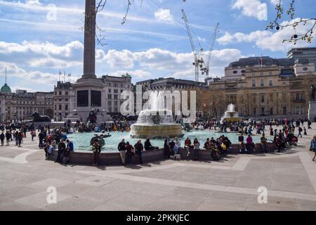 London, Großbritannien. 8. April 2023 An einem warmen Frühlingstag genießen die Menschen den Sonnenschein um die Brunnen am Trafalgar Square. Stockfoto