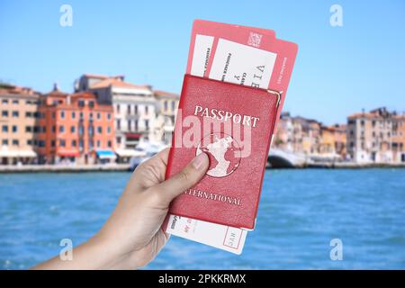 Frau im Besitz eines internationalen Reisepasses mit Bordkarten und wunderschönem Blick auf die Stadt in der Nähe des Meeres im Hintergrund Stockfoto