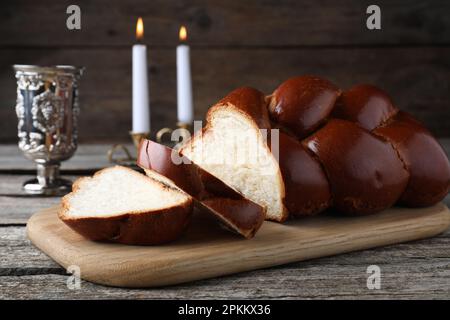 Schneiden Sie hausgemachtes geflochtenes Brot, Becher und Kerzen auf einem Holztisch. Traditionelle Sabbat-Challah Stockfoto