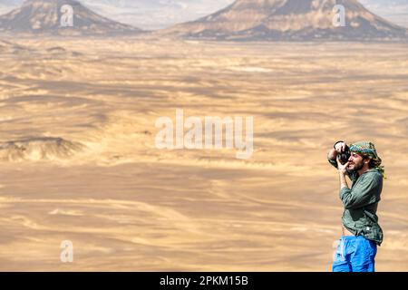 Ein Tourist, der ein Foto auf einem felsigen Felsvorsprung/Basalthügel in der Schwarzen Wüste in Ägypten macht Stockfoto