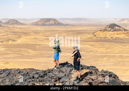 Ein Tourist, der ein Foto auf einem felsigen Felsvorsprung/Basalthügel in der Schwarzen Wüste in Ägypten macht Stockfoto