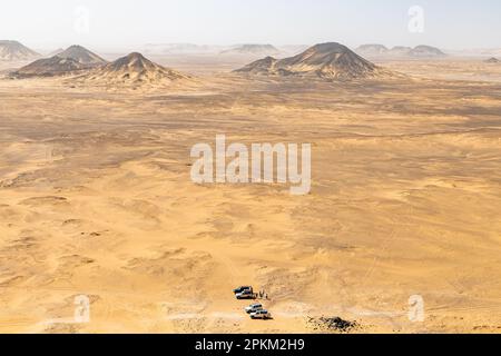 Jeeps parken am Fuße eines Basalthügels auf einem Plateau in der Schwarzen Wüste in Ägypten Stockfoto
