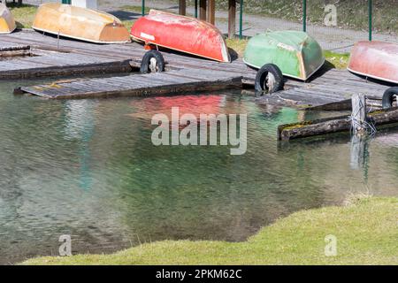 Alte kopfüber liegende Ruderboote auf verwelkten alten hölzernen Hafen vor grünem blühendem Gras als Konzept für alte Schiffe der Schiffstechnik Stockfoto