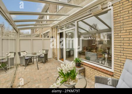 Ein Wohnbereich im Freien mit Terrassenmöbeln und Blumen in den Vasen auf der Seite des Hauses Dach Stockfoto