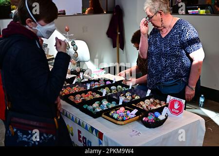 2023 Calgary Farmers' Market: Ein Mädchen in einer Covid-Maske schaut Ostereier an, wenn der Verkäufer im Hintergrund steht Stockfoto