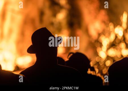 Cottbus, Deutschland. 08. April 2023. Besucher schauen sich das Osterfeuer in Branitz an. Die Kameraden der freiwilligen Feuerwehr des Cottbus Bezirks Branitz hatten etwa 25 Kubikmeter Holzabfälle von den Bewohnern und Handwerkern gesammelt und am Morgen des heutigen Heiligen Samstags auf einen Holzhaufen gestapelt. Mehrere hundert Besucher kamen zum Osterfeuer. Kredit: Frank Hammerschmidt/dpa/Alamy Live News Stockfoto