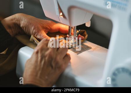 Nahaufnahme der Hände einer älteren Frau mit einer Hausnähmaschine zum Annähen von Fäden an Material Stockfoto