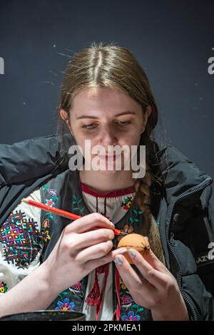 Lemberg, Ukraine. 06. April 2023. Eine junge Frau macht Ostereier. Eine junge Frau in traditioneller ukrainischer Kleidung macht Ostereier mit alter Technologie. Pysanka ist eine alte Tradition, eines der wichtigsten Attribute des Osterurlaubs in der Ukraine, es symbolisiert die Geburt des Lebens. Das Wachs wird mit einem speziellen Stift auf die Eier aufgetragen, und dann wird das Ei in verschiedene Färbungen getaucht. Die wachsgeschützten Teile behalten ihre vorherige Farbe. (Foto: Olena Znak/SOPA Images/Sipa USA) Guthaben: SIPA USA/Alamy Live News Stockfoto