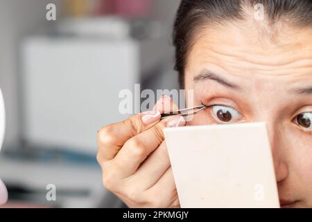 Detaillierte Aufnahme einer Latina-Frau mit einer manuellen Augenbrauenpinzette zur Applikation falscher Wimpern Stockfoto