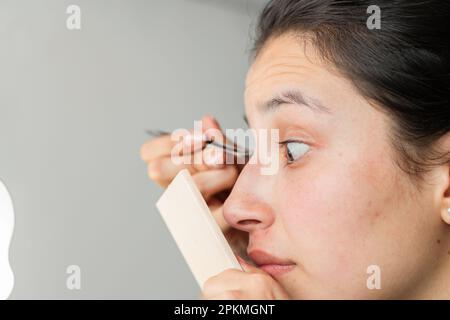 Nahaufnahme des Gesichts einer Latina-Frau, die genau in den Spiegel schaut, um ihre Augen zu bilden. Stockfoto