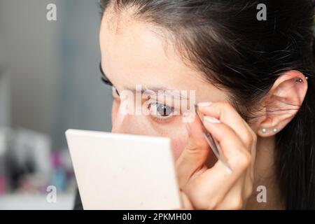 Nahaufnahme eines wunderschönen Latina-Teenagers, der sich mit einer Pinzette die Augenbrauen pflückt Stockfoto