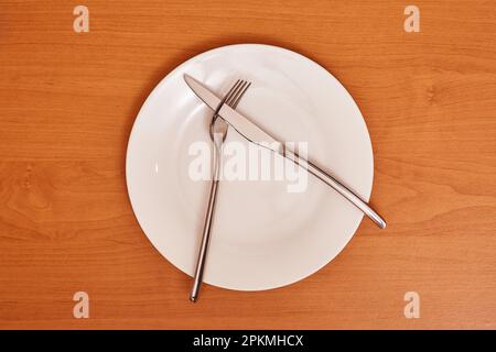 Ein Signal 'mochte das Gericht nicht'. Leeren und reinigen Sie die blaue Platte mit Gabel und Messer auf einem Holztisch als Beispiel für Tischetiketten Stockfoto