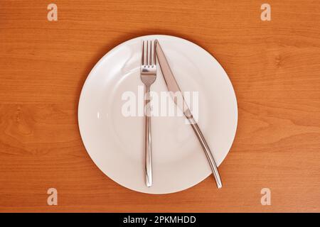 Ein Signal „Es gibt wenig zu essen“. Leeren und reinigen Sie die blaue Platte mit Gabel und Messer auf einem Holztisch als Beispiel für Tischetiketten Stockfoto