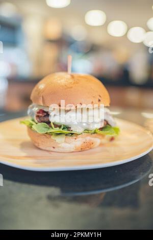 Vertikales Foto von Brot mit Hamburger auf einem Tisch, gefüllt mit Mosarella-Käse, Tomaten und Salat Stockfoto